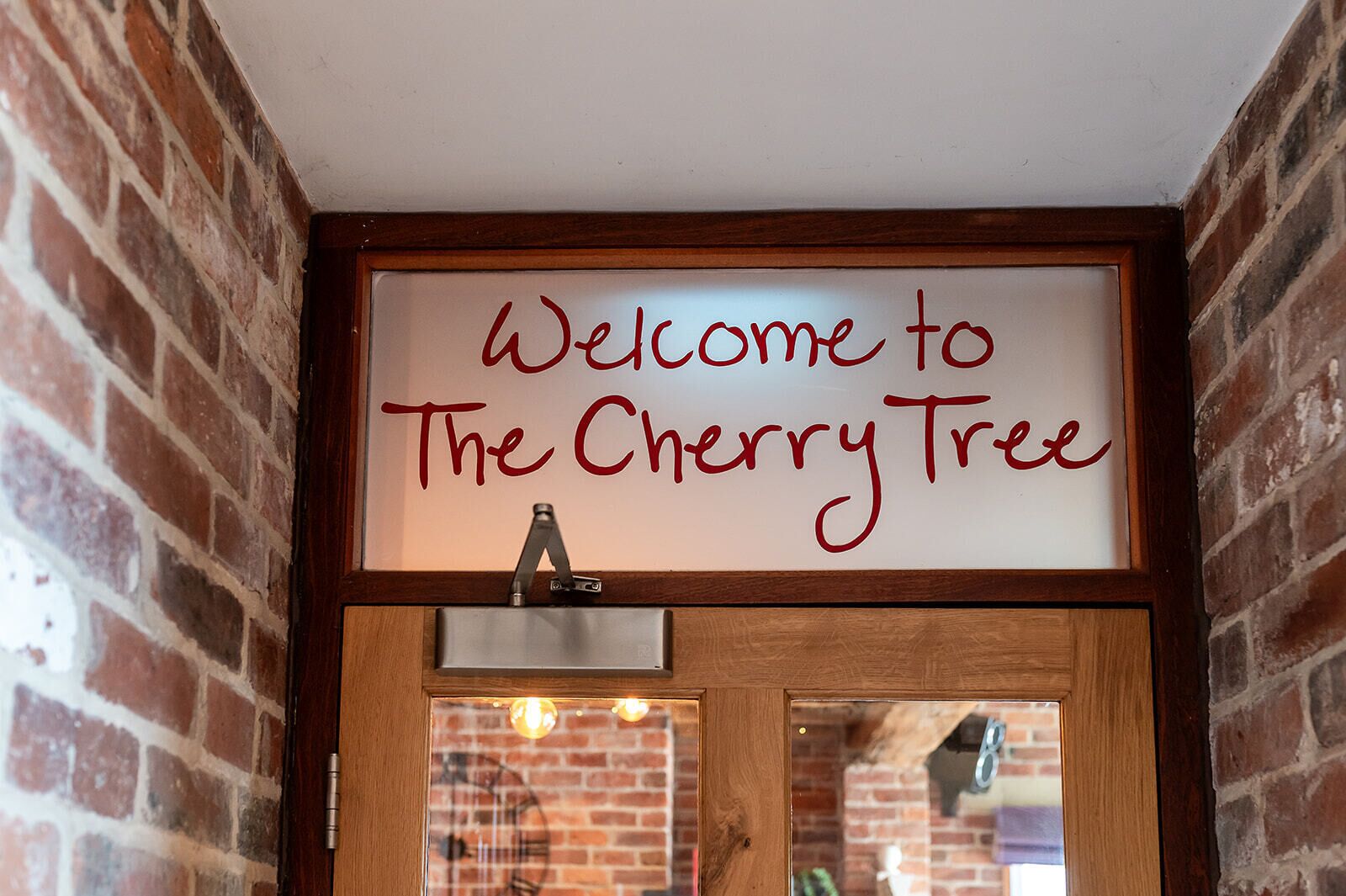 A welcome sign above a wooden door with a metal handle, set against a brick wall.