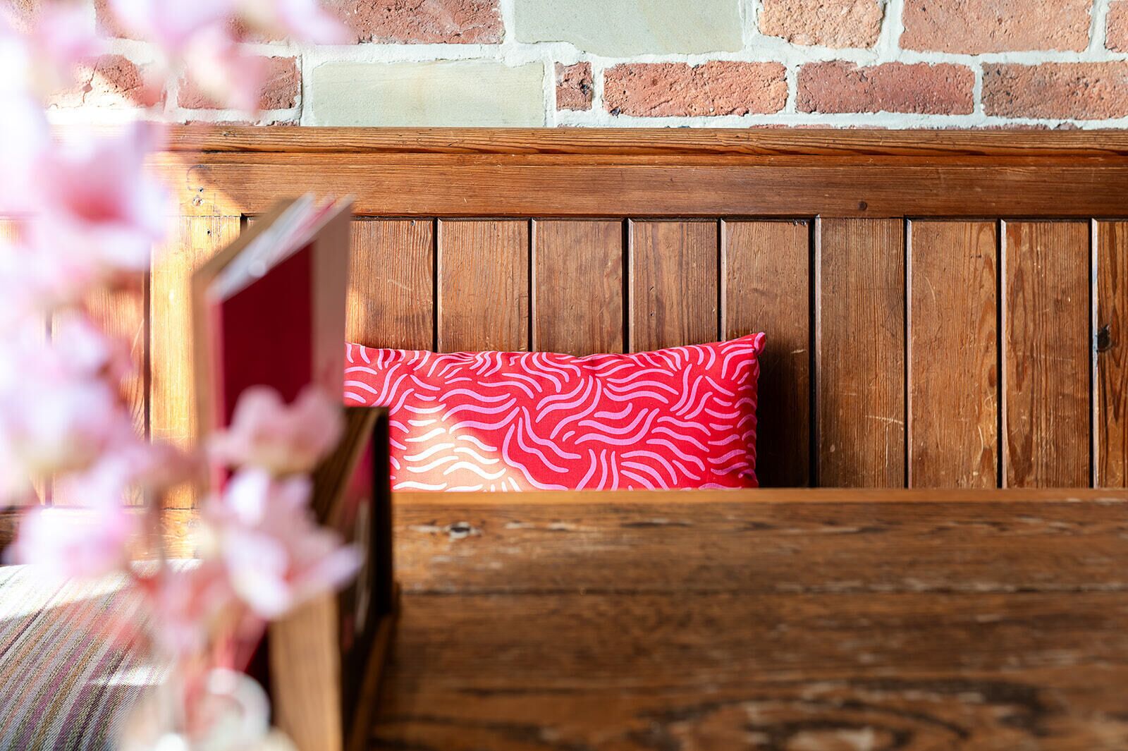 Un banc en bois avec un coussin rouge à motifs, adossé à un mur de briques.