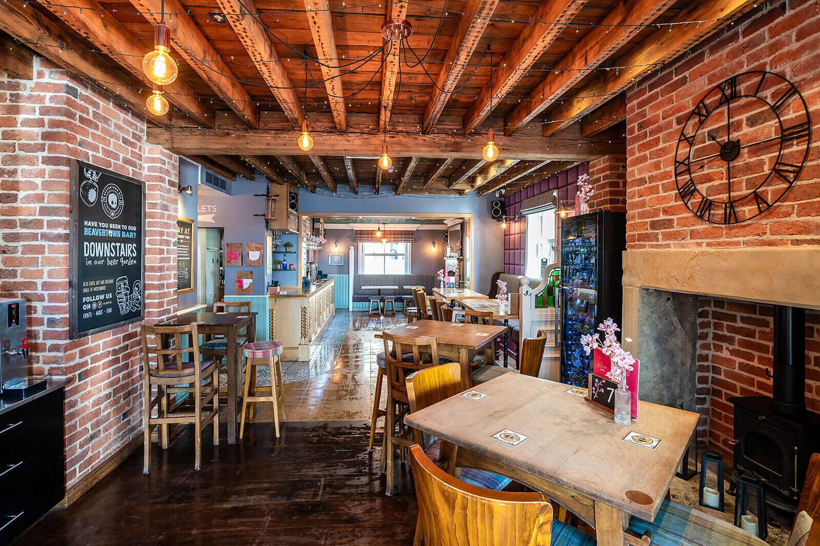 A rustic interior with exposed wooden beams, brick walls, and a bar area with stools and tables.