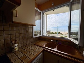 Een keuken met een raam, een spoelbak en een fornuis.