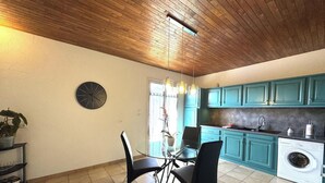 Una cocina con armarios color turquesa, una lavadora, un reloj y un comedor con sillas y una mesa de vidrio.