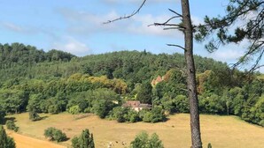 Paisaje rural con una casa rodeada de árboles y campos abiertos.