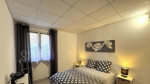 Un dormitorio con cama, ventana con cortinas, radiador, una obra de arte en la pared y lámparas de noche.