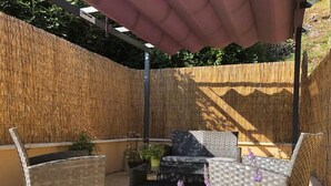 Un patio exterior con mobiliario de mimbre, un muro de bambú y una pérgola que da sombra.