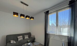 A living room with a grey sofa, a small round table, and a window with curtains. - House with private pool - 2 guests (Auriac-du-Périgord)