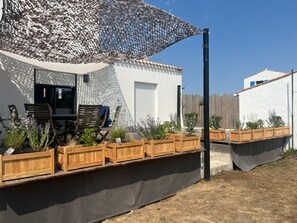 Un espace patio aménagé avec une table et des chaises, des jardinières en bois ornées de plantes et un grand parasol.