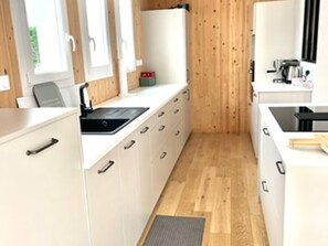 Une cuisine étroite avec des meubles blancs, un évier noir et un plancher en bois.