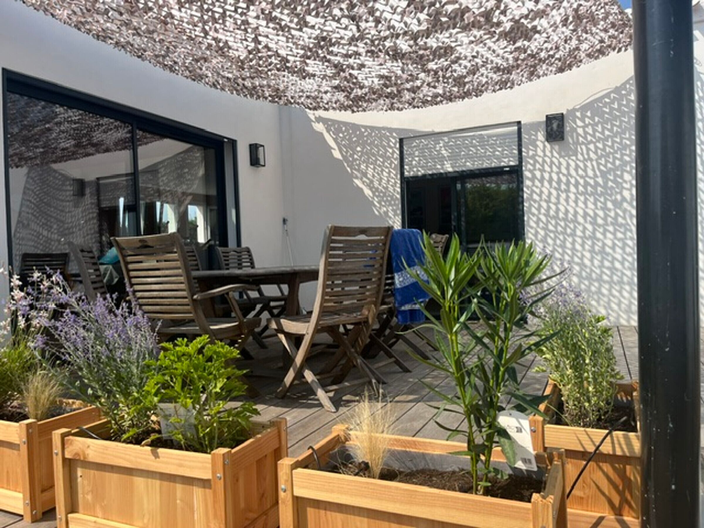 An outdoor patio with wooden furniture, a table, and planters with various plants.
