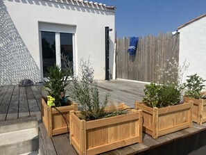 Eine Dachterrasse mit hölzernen Pflanzkästen, in denen verschiedene Pflanzen stehen, ein weißes Gebäude mit einer Tür und ein Holzzaun.