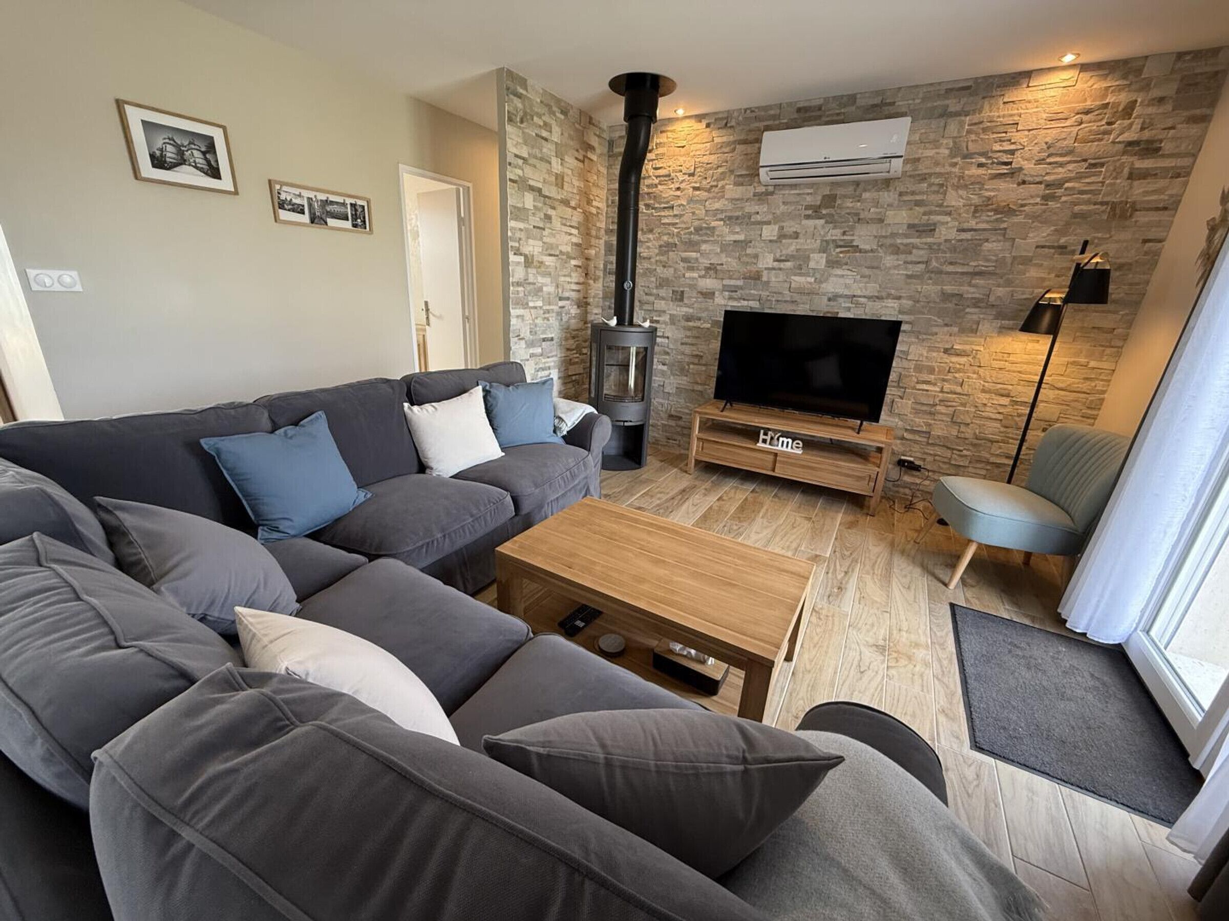 A modern living room with a sectional sofa, a TV on a wooden stand, a fireplace, and stone wall decor.