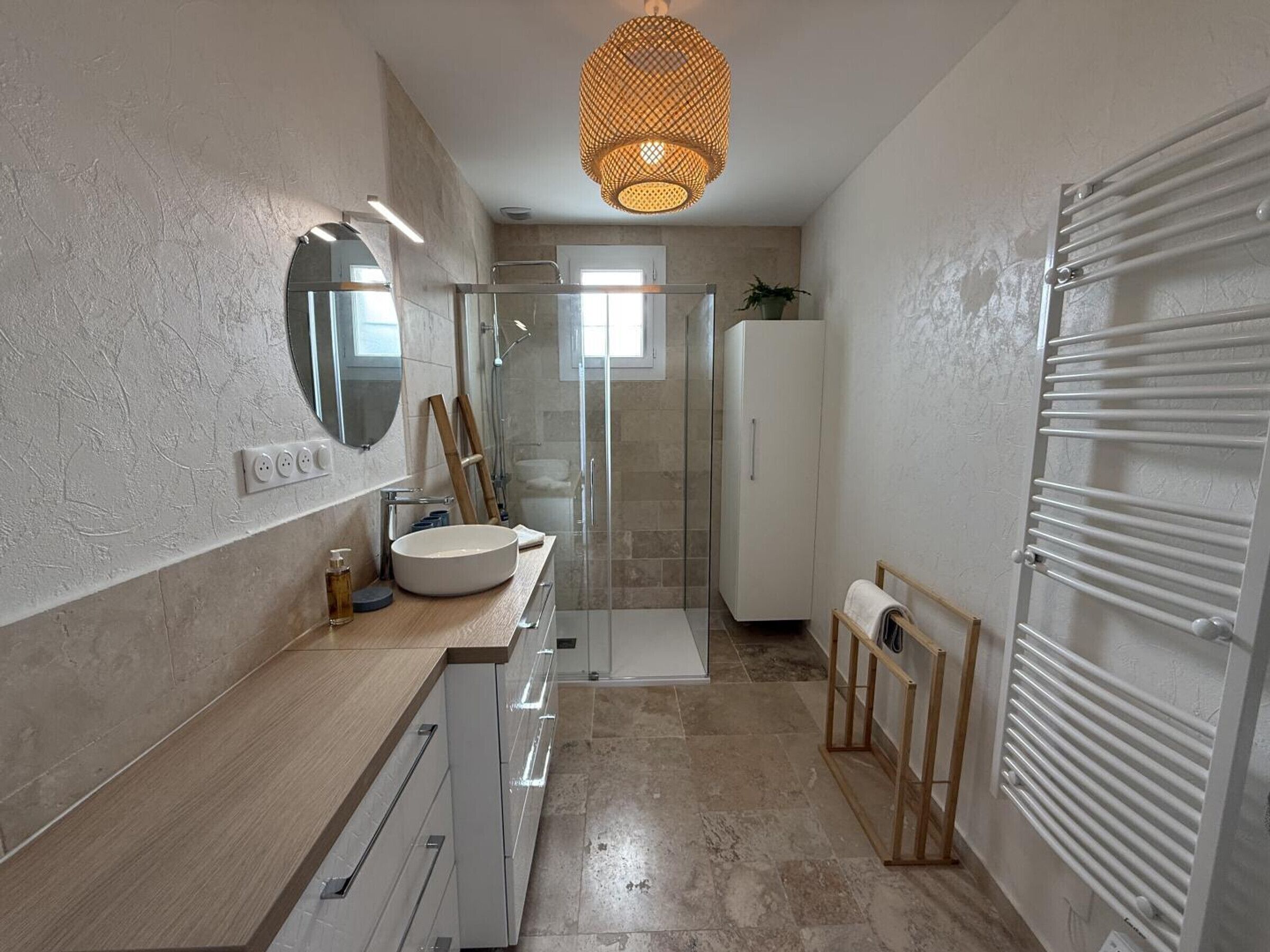 A modern bathroom with a large sink, mirror, shower, and towel rack.