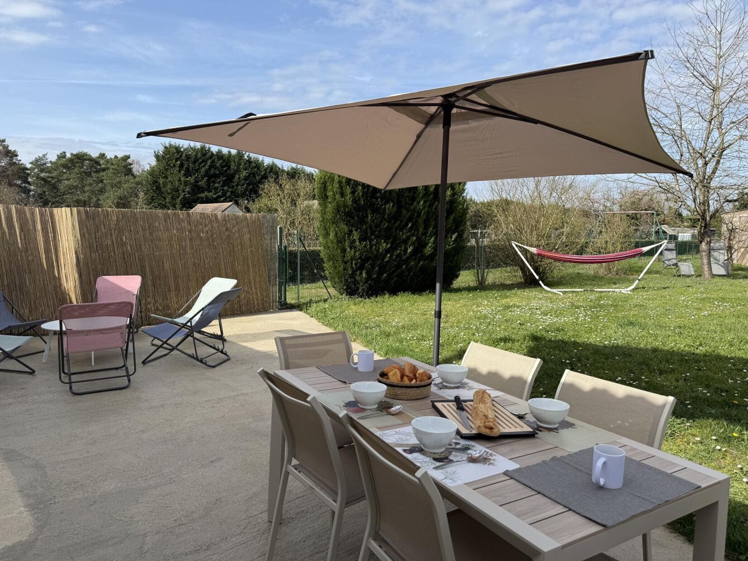 An outdoor patio with a table set for breakfast, surrounded by chairs, and a large umbrella providing shade.