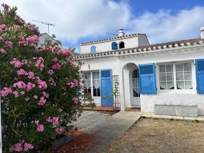 A white building with blue shutters, a small porch, and a garden with pink flowers. - House near sea and woods - 6 guests (La Guérinière)