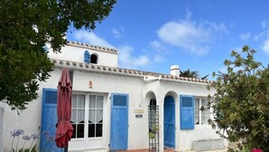 Un bâtiment blanc avec des volets bleus, un petit balcon et un parasol rouge.