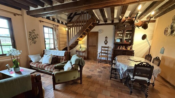 Een gezellige kamer met een houten trap, een bank, een eettafel en een stoel.
