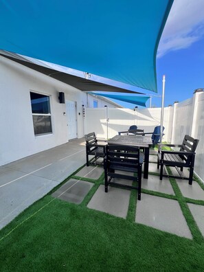 A patio with a table and chairs, a white fence, and a blue awning. - Extended Stay Apt / Wi-Fi, Workspace & Parking (Port St. Lucie)