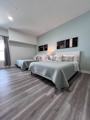 A bedroom with two beds, a window with curtains, and a wall-mounted artwork. - Extended Stay Studio with Spa Rain Shower (Port St. Lucie)