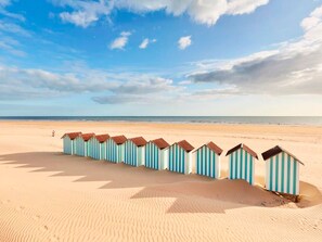 Una hilera de cabañas de playa en una arena clara, bajo un cielo despejado.
