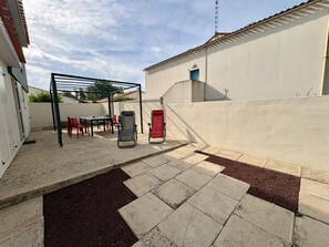 A patio area with a pergola, outdoor seating, and a red chair. - Charming house near forest - 6 guests (Saint-Jean-de-Monts)