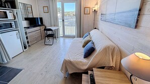 Une pièce compacte comprenant un coin cuisine, un espace repas, un canapé avec des coussins, une télécommande et une lampe.