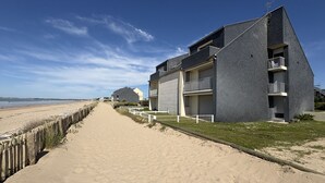 Un hôtel situé en bord de mer, avec un chemin piétonnier de sable, une clôture en bois et un ciel dégagé.