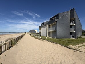 Ein Strandhotel mit sandigem Weg, Holzzaun und blauem Himmel.