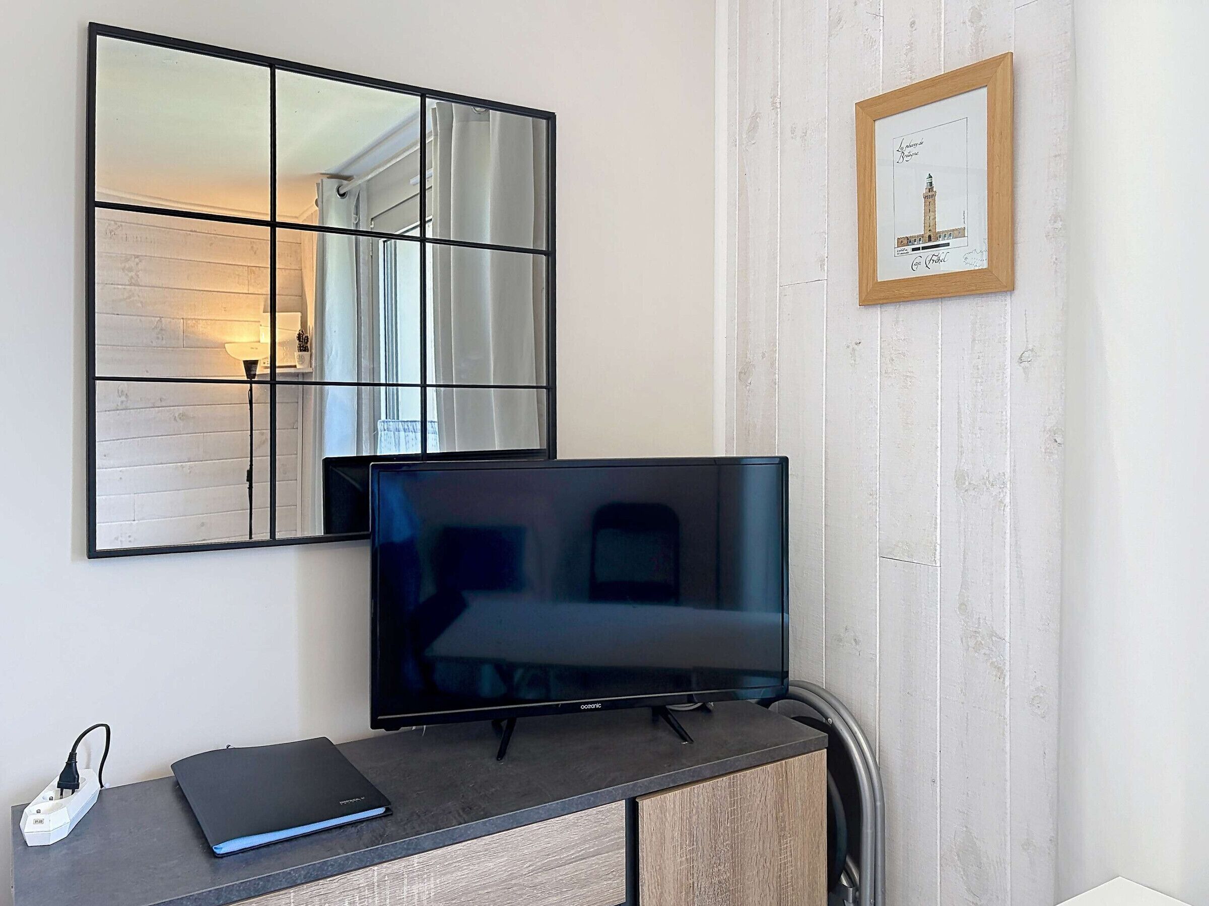 Uma televisão em um suporte, um régua de tomadas, um laptop e um quadro na parede.
