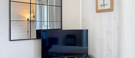 TV-taso, jatkojohto, kannettava tietokone ja seinällä oleva kehystetty kuva.