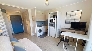 Une pièce compacte comprenant un lit, une petite kitchenette, un lave-linge, une télévision et un bureau.