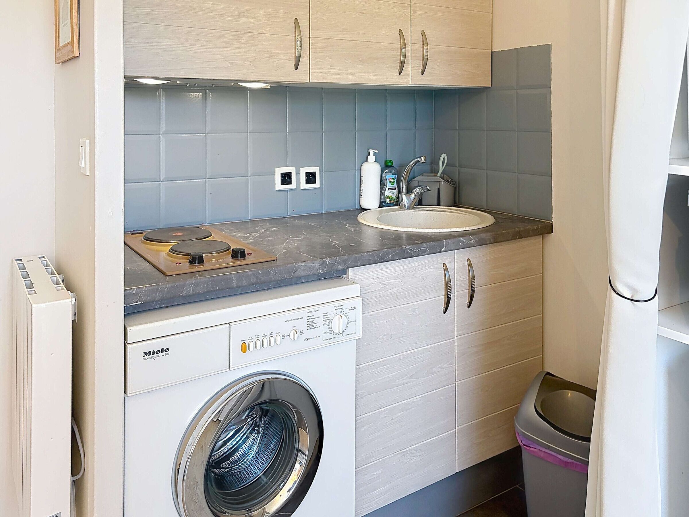 A compact kitchen with a built-in washing machine, a sink, and cabinets.