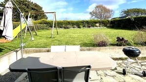 Eine Terrasse mit Tisch, Stühlen, einer Schaukel und einem Grill.
