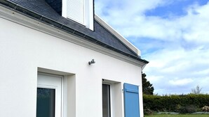 Ein weißes Gebäude mit Fenster, Fensterläden, einer Tür und einem Grill vor der Fassade.