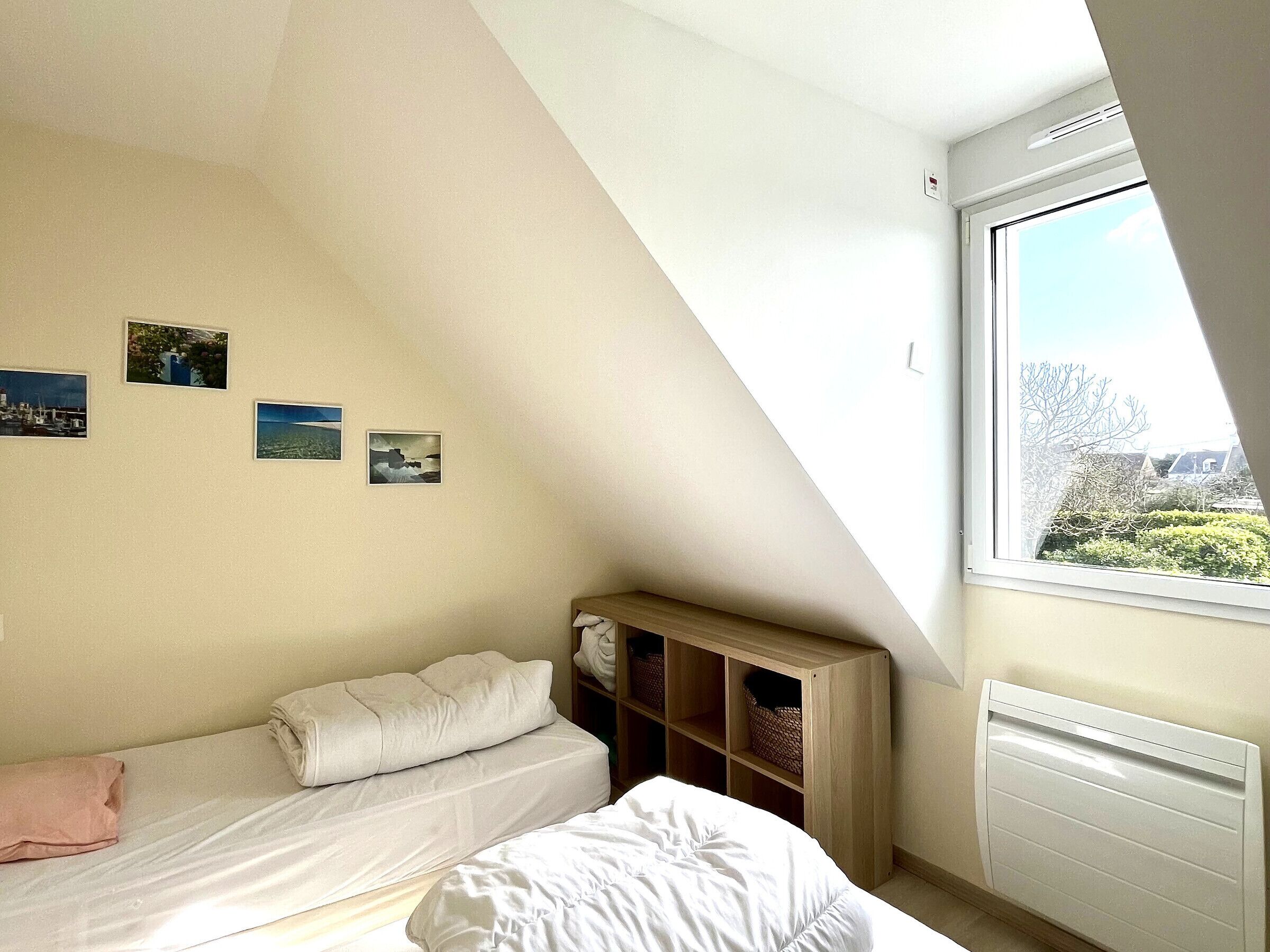 Une chambre avec un plafond en pente, un lit, une fenêtre donnant sur un paysage agréable et un radiateur.