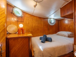 A compact, wood-paneled room with a bed, a small table with a lamp, and a mirror.