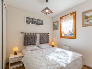 Ein Schlafzimmer mit einem Bett, zwei Nachttischlampen, einem Fenster mit Ausblick und einer Deckenleuchte.