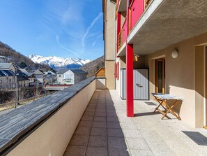 Ein Balkon mit Blick auf schneebedeckte Berge, eine rote Tür und ein kleiner Tisch.