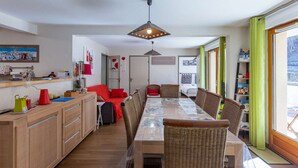 A modern kitchen with wooden cabinets, a dining table with chairs, and a view of the outdoors through large windows. - Apartment near village - 10 guests (Barèges)