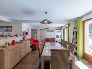Eine moderne Küche mit Holzausstattung, einem Esstisch mit Stühlen und Blick ins Freie durch große Fenster.