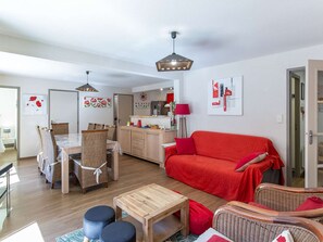 Ein modernes Wohnzimmer mit einem roten Sofa, einem Holzesstisch, Korbstühlen und einer Küche im Hintergrund.
