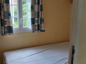 Une chambre avec un lit simple, une fenêtre avec des rideaux et une porte.