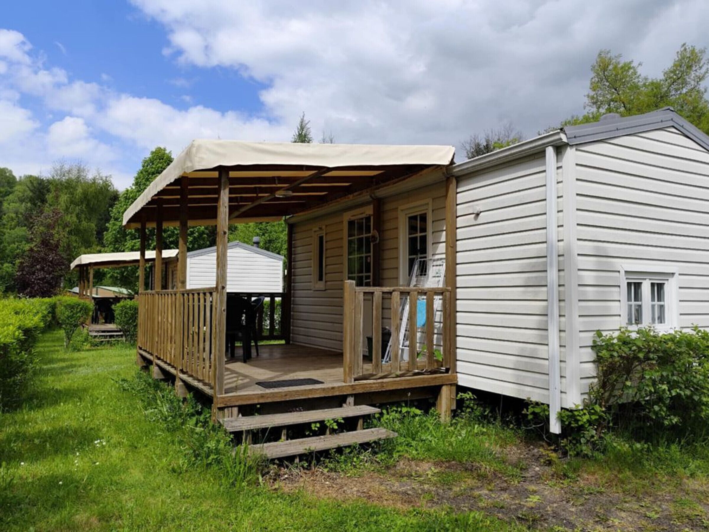 Une cabane en bois d’un seul étage, dotée d’un porche, d’une terrasse couverte et d’un petit abri attenant.