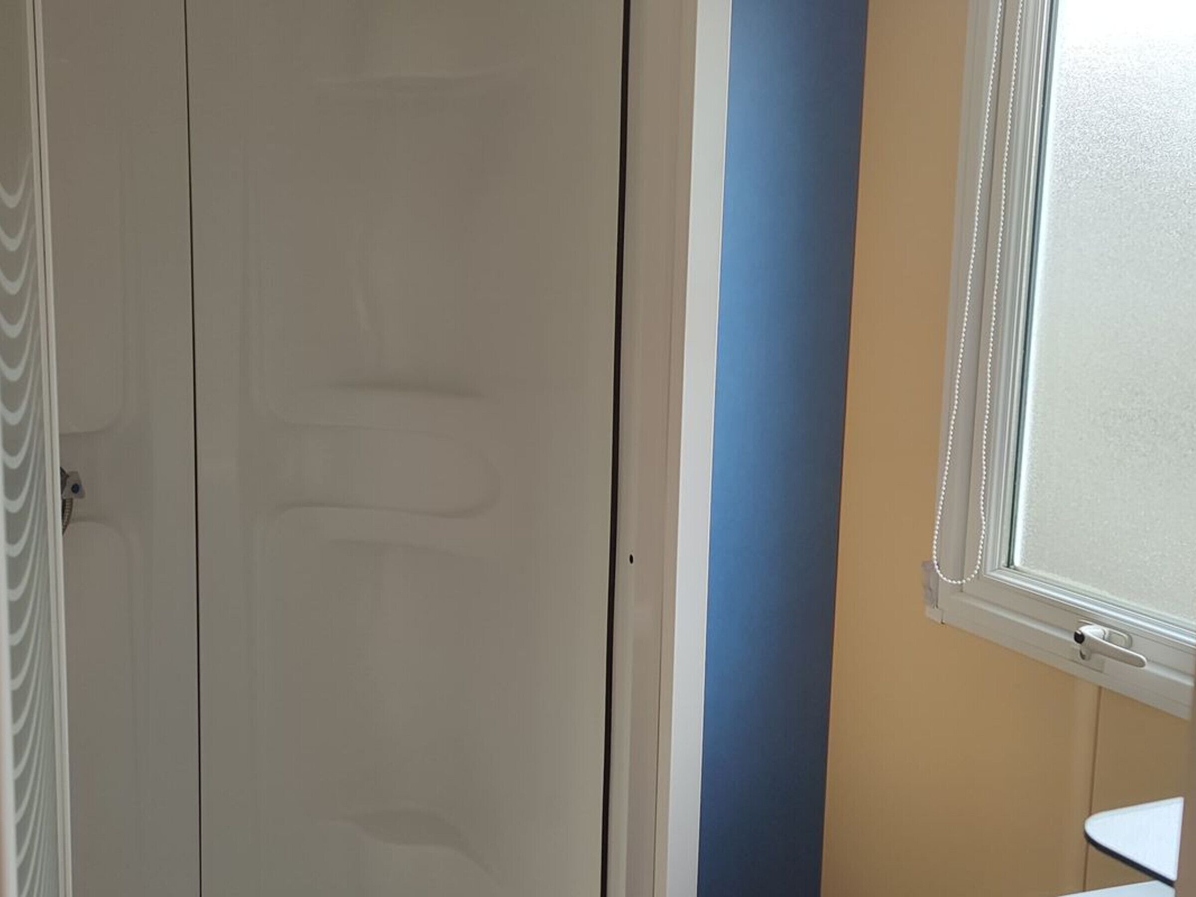 Ein Zimmer mit geschlossener Tür, einem Fenster mit weißem Rahmen und einem Teil eines blauen Streifen an einer Wand.