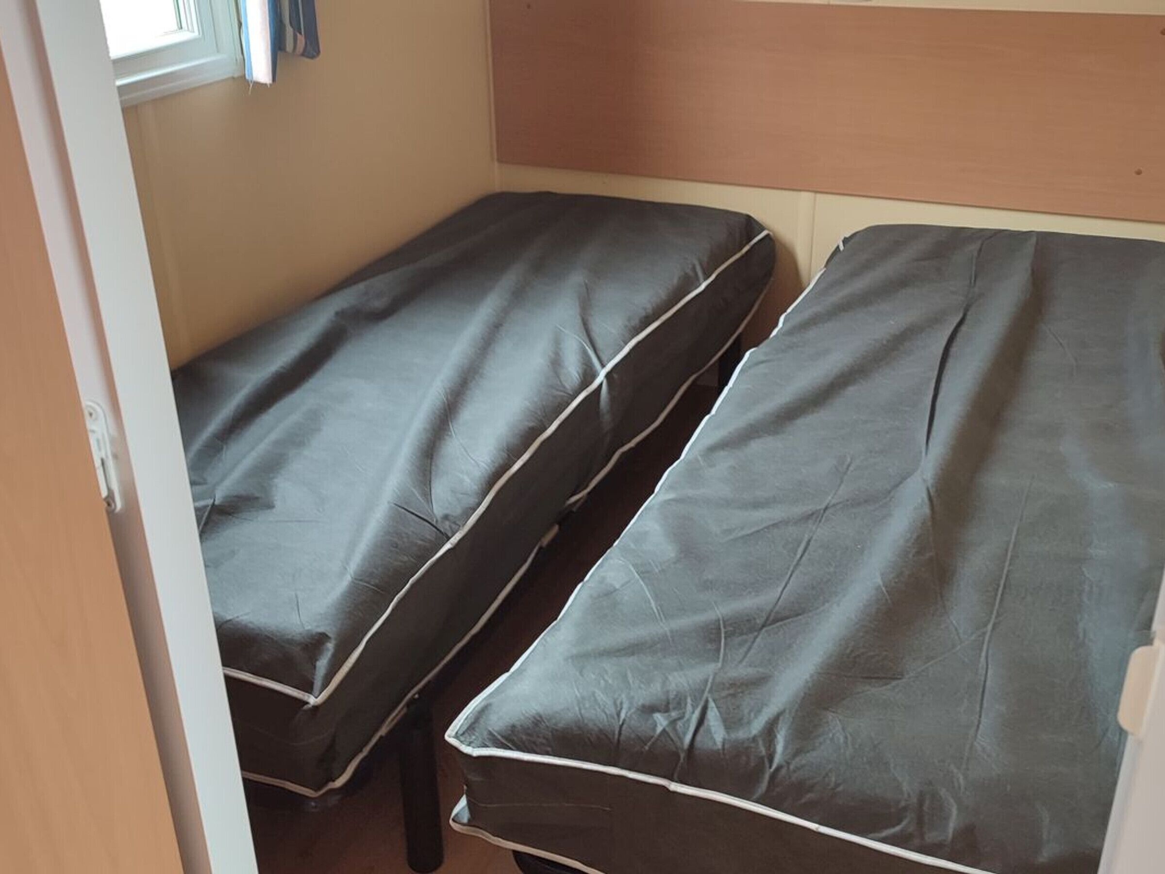 Una habitación pequeña con dos camas individuales, una ventana con cortinas y un cabecero de madera.