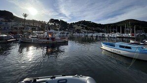 En småbåtshamn med förtöjda båtar, stilla vatten och ett kuperat landskap i bakgrunden.