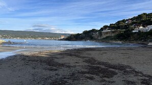 En kustnära strand med en stenig strandlinje, en klar himmel och byggnader på en sluttning.