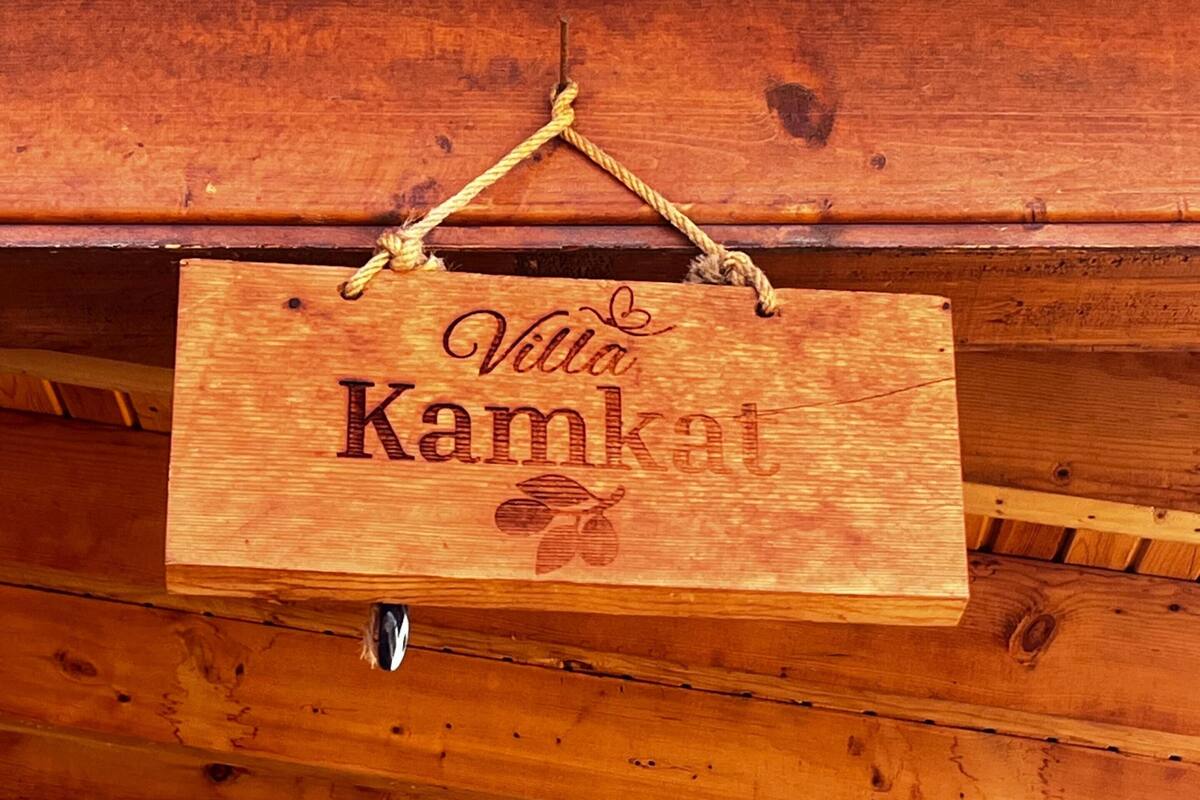 A wooden sign with the text 'Villa Kamkat' hanging from a ceiling beam.