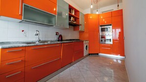 A kitchen with orange cabinets, a stainless steel oven, and a washing machine. - Livia's Vatican House - Metro Aurelia (Rome)