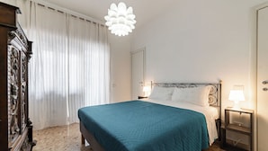 A bedroom with a bed, a nightstand, a dresser, a window with curtains, and a chandelier. - Livia's Vatican House - Metro Aurelia (Rome)