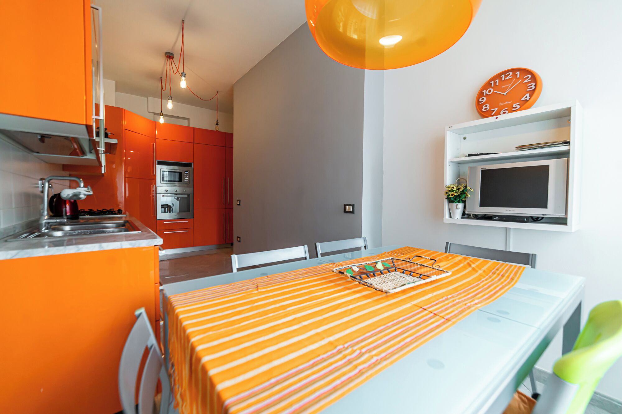 Eine moderne Küche mit orangefarbenen Schränken, einem eingebauten Ofen und einem Essbereich mit gestreiftem Tischläufer.