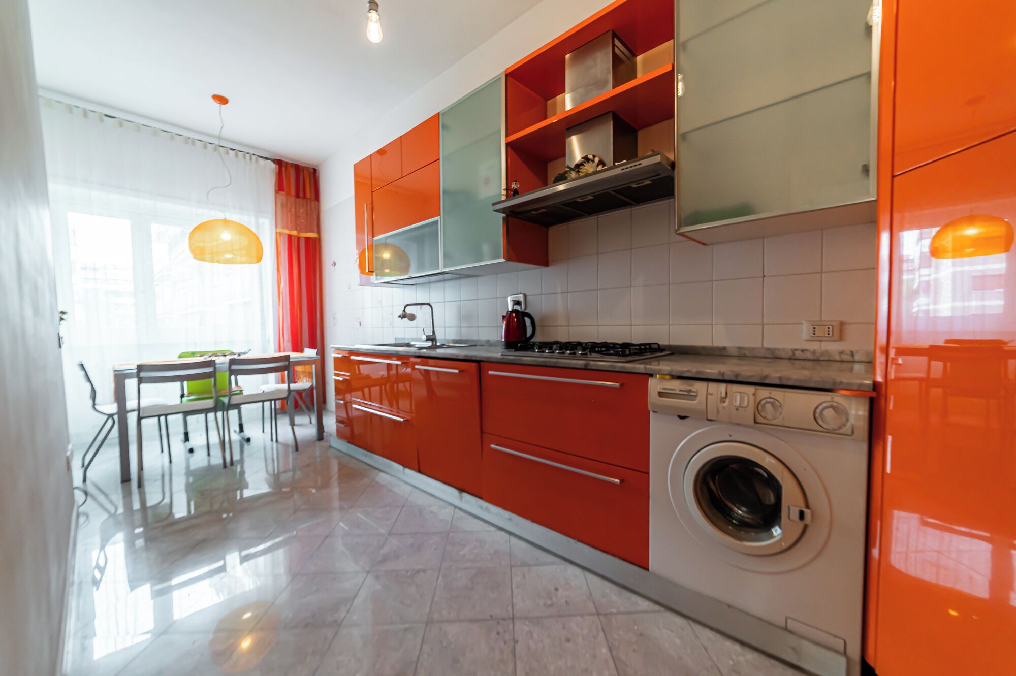 Una cocina moderna con gabinetes rojos, lavadora integrada y comedor con mesa y sillas.